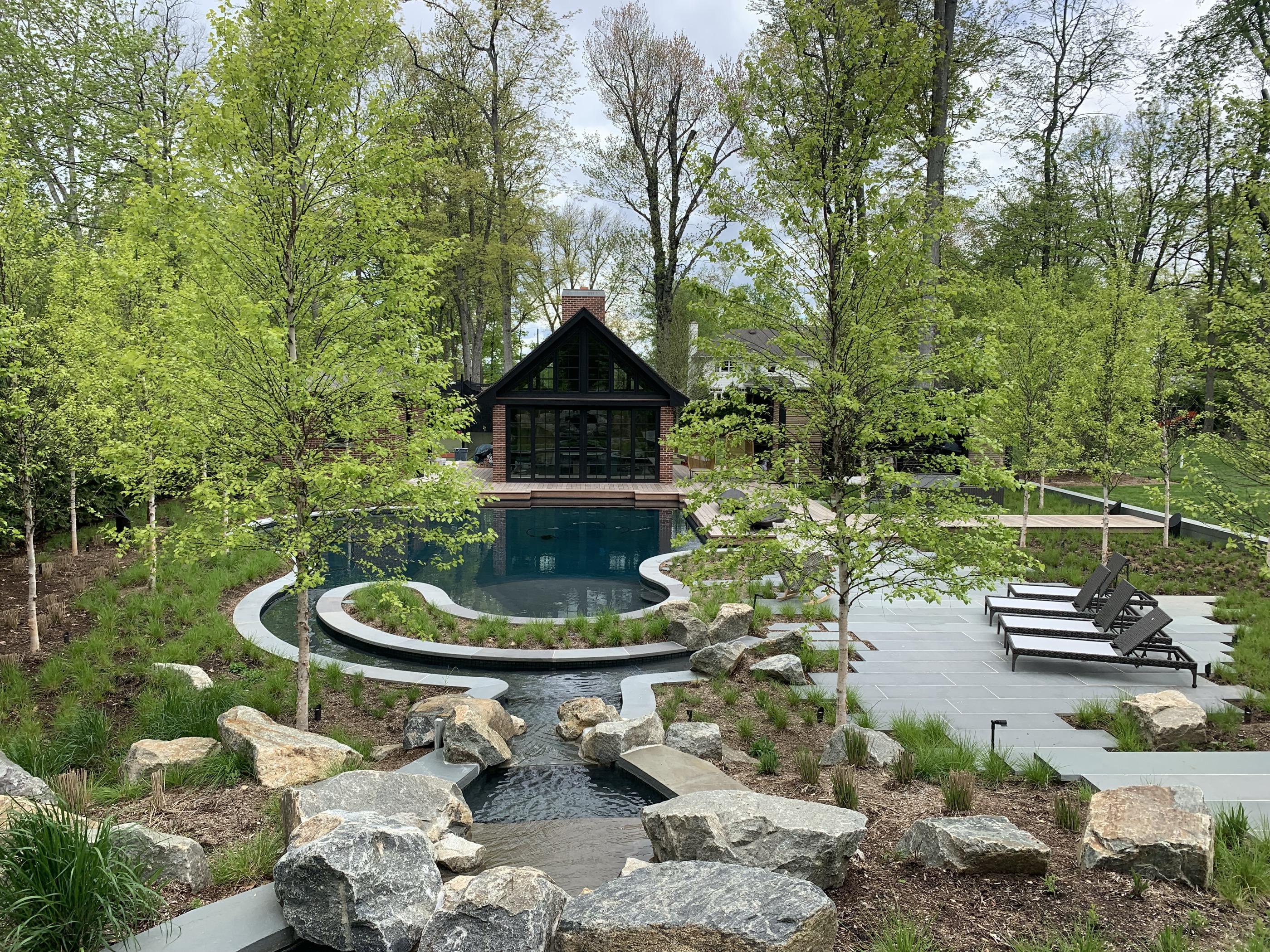 Freeform pool with stone stream feature and modern black pool house