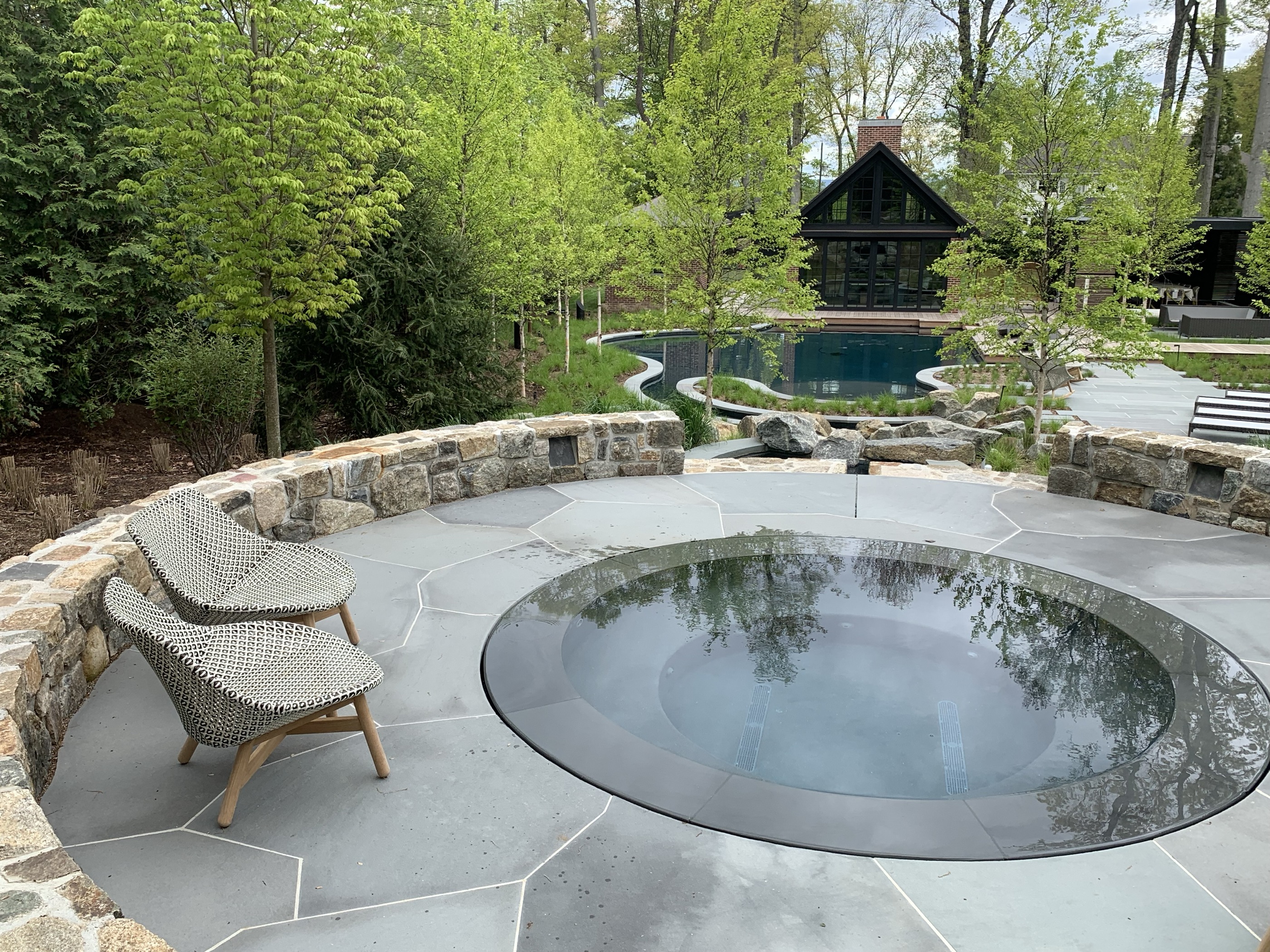 Round inground spa with stone wall and freeform pool background