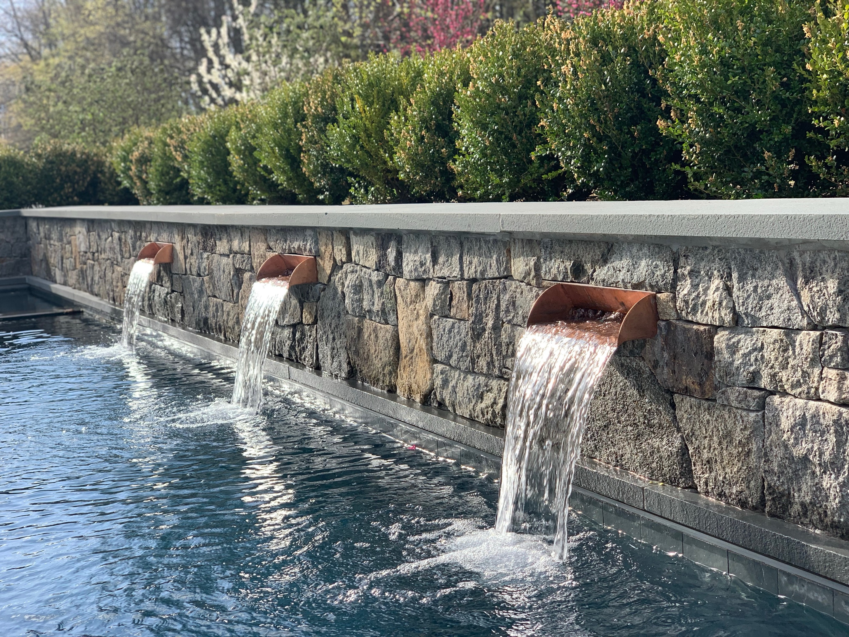 Three copper scuppers spilling into pool against stone wall